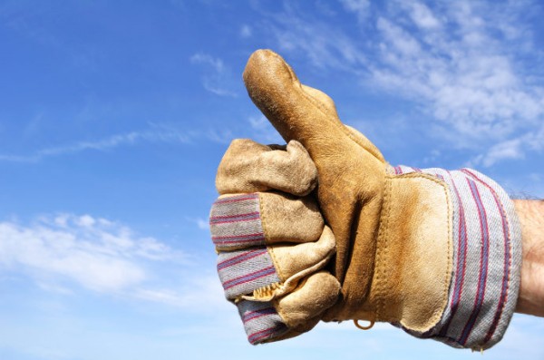 Arbeitshandschuh zeigt den Daumen hoch vor einem blauen Himmel