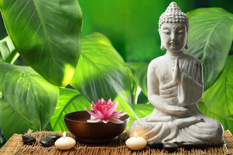 Sitzende Buddha Figur vor grünem Blätter-Hintergrund
