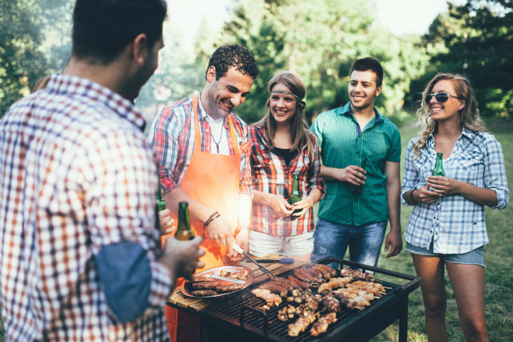 Freunde stehen um einen Grill versammelt der voll mit Grillgut ist