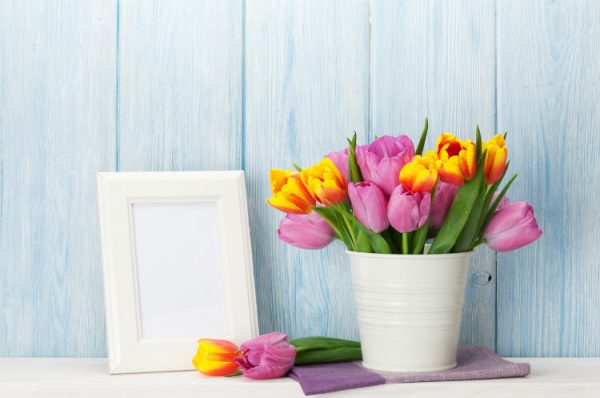 bunte Tulpen in einer weißen Vase neben einem weißen leeren Bilderrahmen
