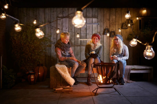 Drei Jugendliche sitzen auf einer schön dekorierten Terrasse im Winter an einem kleinen Lagerfeuer