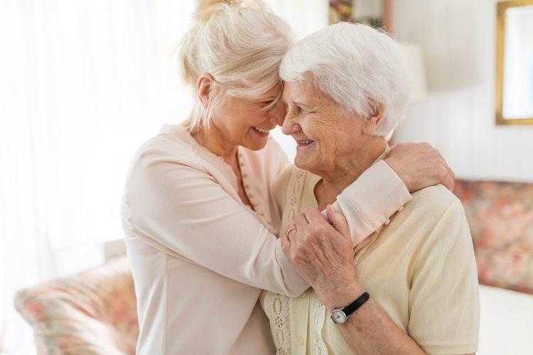 Eine jüngere Frau umarmt eine ältere Frau, beide lächeln glücklich