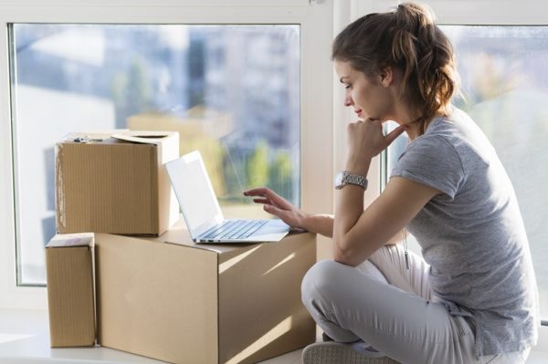 Junge Frau sitzt vor Umzugskartons und Laptop