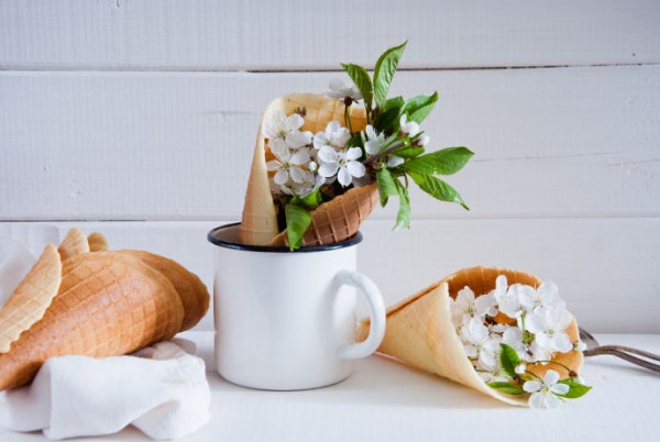 Frische Blumen in Eiswaffeln und einem Behälter vor einer hellen Wand