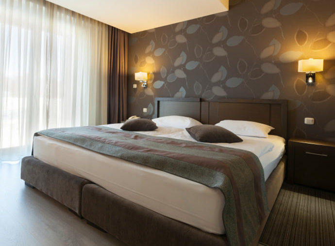 Boxspringbett in einem Raum mit zugezogenen durchsichtigen Gardinen.