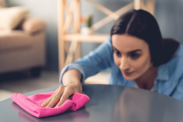 Frau wischt Staub mit einem Lappen von einem Tisch