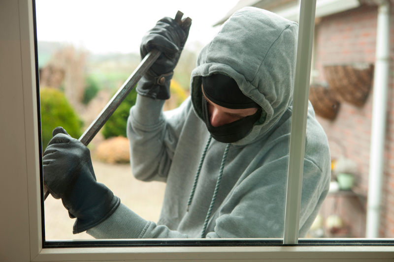 Ein vermummter Mann bricht ein Fenster auf