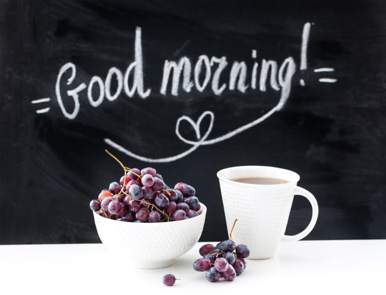 Schriftzug auf einer Tafelwand mit einer Tasse Kaffee und einer Schale Früchte.